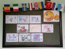 Tablica z karteczkami ukazująca grafiki oraz zwroty dotyczycące poszukiwania pracy w różnych językach. Nad tablicą flagi państw europejskich.